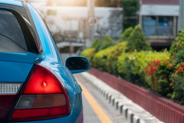 Wall Mural - Luxury rear corner of blue car on the road. With Trees planted on the side of the road and the blur of the city. Open brake light.