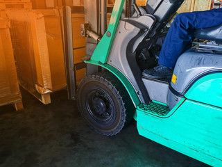 Worker driving forklift loading and unloading shipment carton boxes and goods on wooden pallet from container truck to warehouse cargo storage in logistics and transportation industrial 