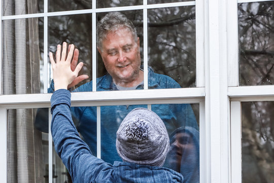 teen visiting senior citzen quarantined in home, touching hands through the window