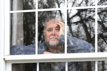 Smiling senior man standing at the window looking out