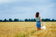 © Elena  - A girl with brown hair walks through a wheat field, holding a hat in her hand. The view from the back. Rural landscape. Autumn mood.