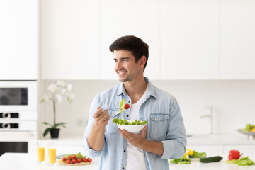 Smiling man with plate of salad fresh vegetables on modern kitchen at home.