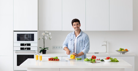 Wall Mural - Happy young man preparing cooking healthy vegan food cut salad in kitchen.