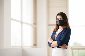 An Asian working woman wearing a black mask stands at the office.