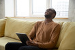 © fizkes - Cheerful black man laughing while watching videos or blogger stream online on digital tablet. Joyful guy using touch pad happy entertaining or getting good news sitting on sofa in living room