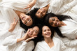 © fizkes - Top view five diverse women in white bathrobes lying in bed smile look at camera feels happy after body treatment, day spa procedures, resort beauty salon satisfied clients, bachelorette party concept