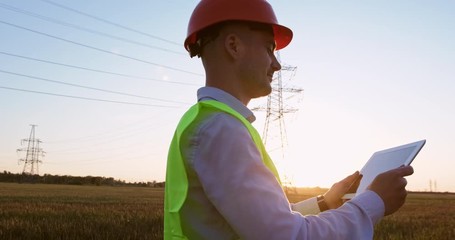 Wall Mural - a worker with an electronic tablet walks along the road in front of a high-voltage power line and ta