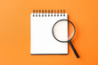 Magnifier glass and empty notebook on orange background, flat lay with space for text. Find keywords concept