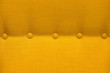 Texture of a close-up of a yellow fabric upholstery of an armchair with elements of accessories, background.