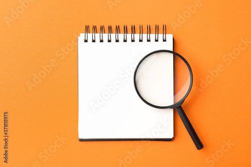 Fotografía Magnifier glass and empty notebook on orange background, flat lay with space for text