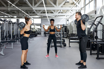 Wall Mural - professional sportsman teach girls to pump muscles with the use of weights, gives instructions on how to perform the exercises correctly