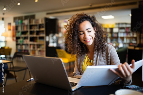 Cuadros en Lienzo Young afro american woman sitting at table with books and laptop for finding inf