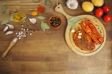 raw meat, two meat pickled in spices meat medallions on a round wooden board on the table, garlic, bay leaf, potatoes and tomatoes nearby, cooking concept, copy space