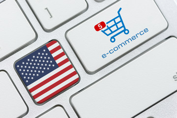 Wall Mural - Online shopping / home shopping / product ordering, ecommerce concept : Flag of USA, shopping cart with a word e-commerce on a computer keyboard, depicting buyer buys goods or things via the internet