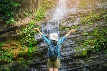 Asian girl tourist traveling adventure exploring nature jungle trail into forest waterfall open arms in success and peace, wearing travel gear bag hat, summer hot healthy outdoor freedom lifestyle