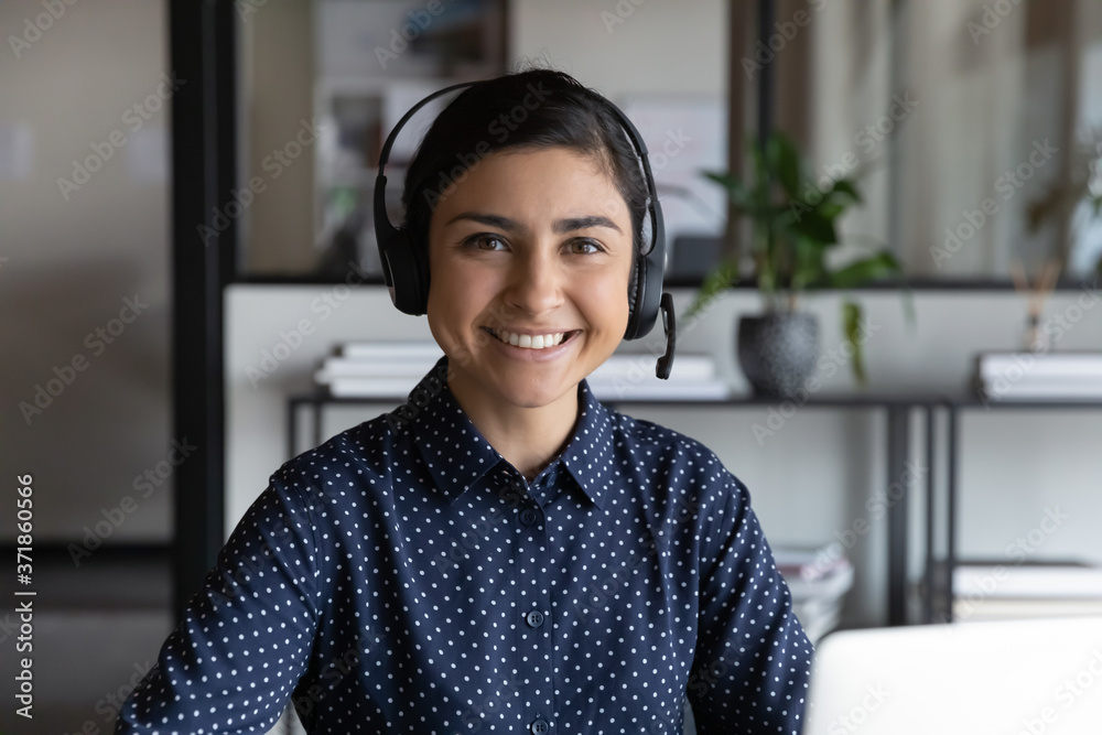 Head shot portrait of pleasant smiling young indian ethnicity attractive female employee wearing wireless headset with mic, professional consultant advisor hotline specialist looking at camera. - obrazy, fototapety, plakaty 