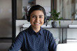 Head shot portrait of pleasant smiling young indian ethnicity attractive female employee wearing wireless headset with mic, professional consultant advisor hotline specialist looking at camera.