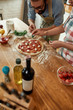 © Svitlana - For a tasty pizza. Young couple making pizza together at home. Man in apron, professional cook adding mozzarella cheese on the dough while woman helping him adding basil. Hobby, lifestyle