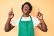 © Krakenimages.com - Handsome african american man with afro hair wearing waiter apron amazed and surprised looking up and pointing with fingers and raised arms.