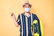© Krakenimages.com - Young handsome man wearing medical mask holding suitcase smiling happy pointing with hand and finger to the side