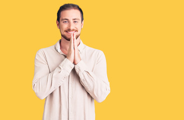 Young handsome caucasian man wearing casual clothes praying with hands together asking for forgiveness smiling confident.