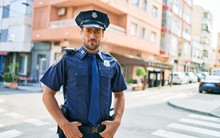 Young Handsome Hispanic Policeman Wearing Police Uniform. Standing With Serious Expression At Town Street.
