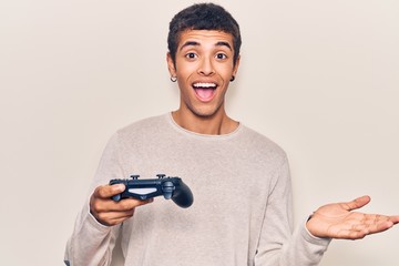 Young african amercian man playing video game holding controller celebrating achievement with happy smile and winner expression with raised hand