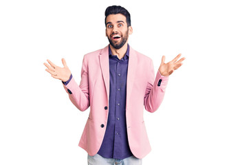 Young handsome man with beard wearing elegant jacket celebrating victory with happy smile and winner expression with raised hands