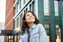 Confident Happy Beautiful Young Hipster African American Woman Wearing Denim Jacket Looking Up Standing On City Street Outdoors Dreaming, Thinking Or Good Future On Urban Buildings Background.