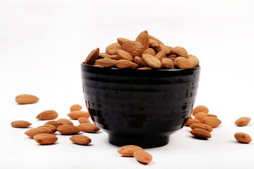 Group of almonds inside and outside bowl isolated on white.