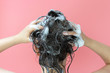 © TATIANA KIM - A girl washes her hair with shampoo on pink background, rear view