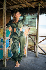 Wall Mural - Young pretty woman standing barefoot on wooden deck and smiling. Hair and clothes are blown by the wind. Vacation concept. Travel to Asia. Bali, Indonesia