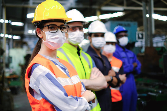 Industrial woman engineer or factory worker wearing helmet and hygiene face mask with men stand in line at manufacturing plant.People working industry during covid pandemic.