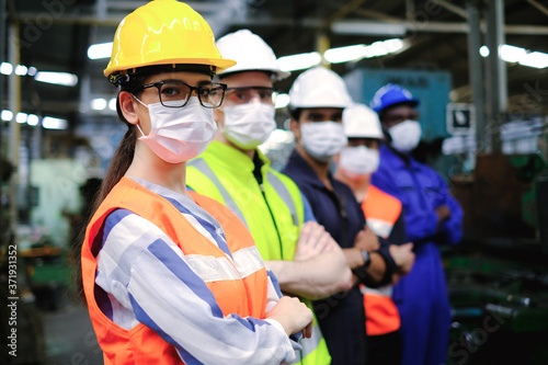 Cuadros en Lienzo Industrial woman engineer or factory worker wearing helmet and hygiene face mask with men stand in line at manufacturing plant