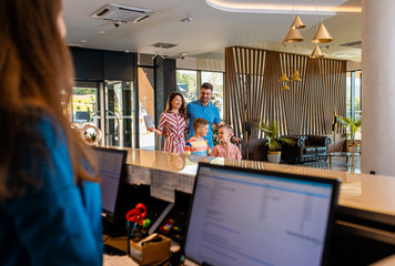 Smiling family of four in the hotel lobby check in at the reception for vacation.