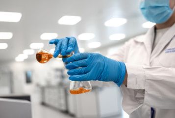 Flasks with brown liquid in scientist hands with dropping chemical liquid to test tubes, science and medical research and development concept