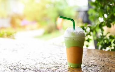 Matcha green tea with milk on plastic glass on the wooden table and nature green background - Green tea smoothie