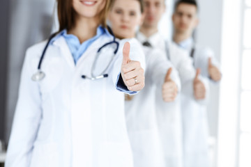 Wall Mural - Group of modern doctors standing as a team with thumbs up in hospital office. Medical help, insurance in health care, best desease treatment and medicine concept