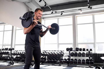 young muscular man in sportswear lift weights while working out in gym, strong guy exercises alone