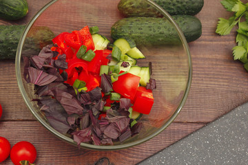 Making salad of fresh vegetables and herbs in a glass bowl on a wooden table.