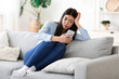 © Prostock-studio - Bored At Home. Weary Asian Girl Sitting With Smartphone On Sofa