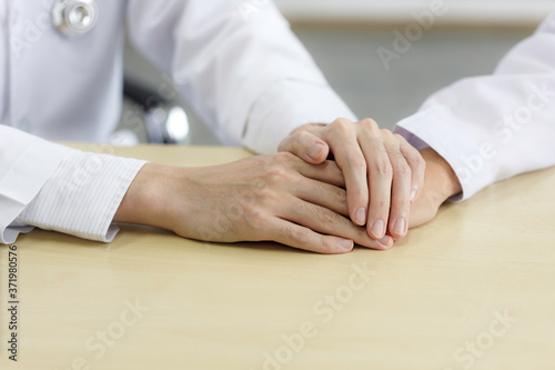 Close up male doctor\'s hands holding female d’octor’s hand for encouragement and empathy. Medical psychology in encouraging and reducing the negative effects of sick people.