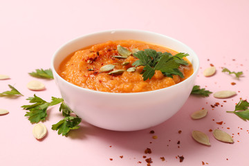 Composition with bowl of pumpkin soup on pink background, close up