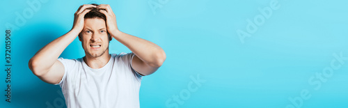 Fotografía Horizontal crop of angry man with hands near head looking at camera on blue back