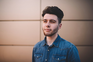 Handsome pensive hipster guy with trendy hairstyle looking thoughtfully away standing outdoors, young caucasian man in blue denim shirt dreaming about successful future concentrated on idea