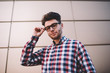 © BullRun - Portrait of handsome male clever student in eyeglasses posing on wall background, positive hipster guy dressed in stylish shirt and spectacles for vision correction looking at camera smiling