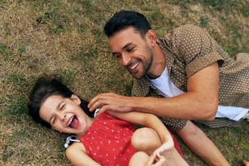 Wall Mural - Top view of a cheerful father playing with his daughter on the grass outdoors. Dad enjoying at day out with his child in the park. Daddy and daughter share love. Happy father's Day.