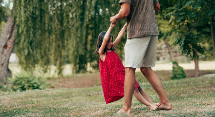 Wall Mural - Horizontal image of daughter dancing with father outdoors. Ñute little girl playing with her loving dad in the park. Daddy and kid having fun together. Happy father's day.