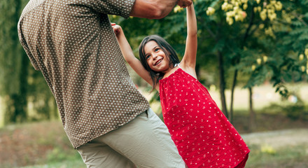 Wall Mural - Cropped image of smiling happy daughter spinning with her .father outdoors. Ñute little girl playing with her loving dad in the park. Daddy and kid having fun together. Happy father's day.