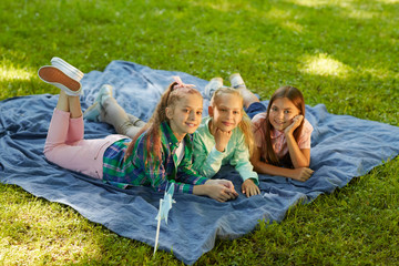 Wall Mural - High angle portrait of three teenage girls smiling at camera while lying on green grass in park outdoors lit by sunlight, copy space